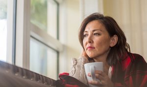 woman peacefully looking out window with cup of coffee stressing importance of brain health